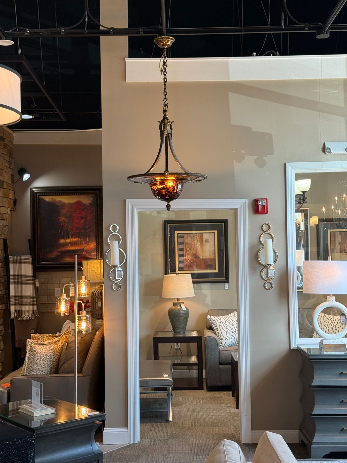 A chandelier hangs in a room with neutral walls, doorway to a furnished space.