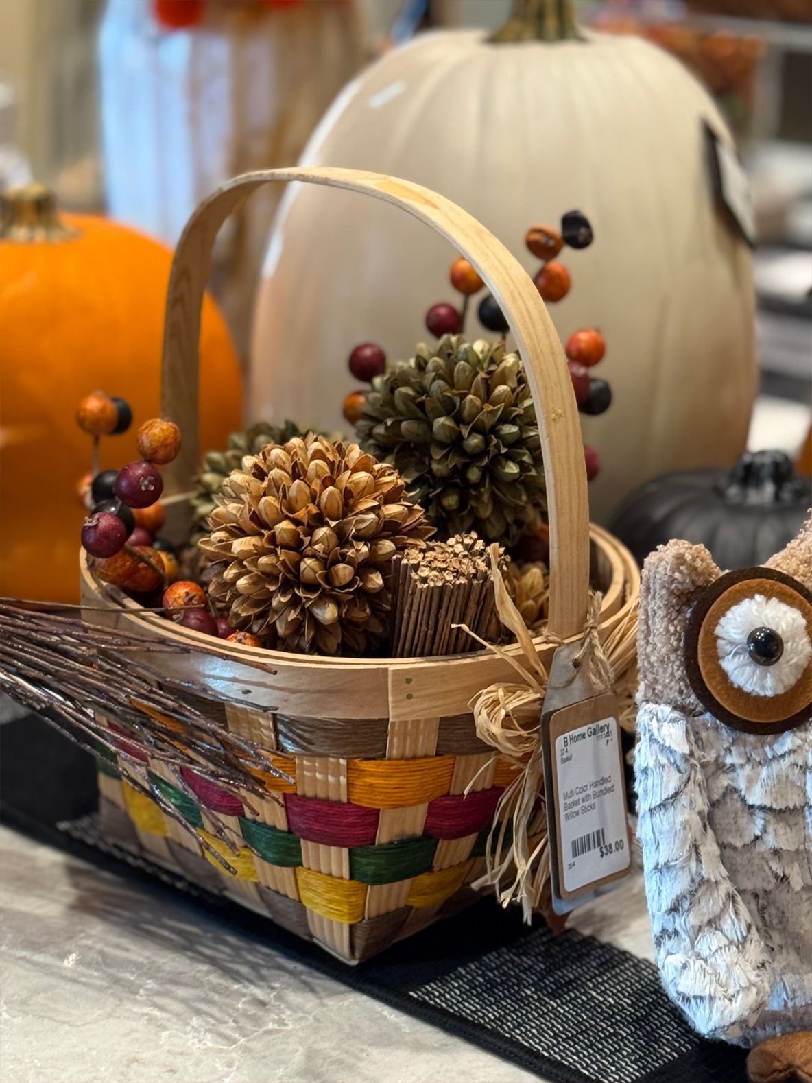 Basket of fall decor: pumpkins, gourds, berries, and an owl on a table.