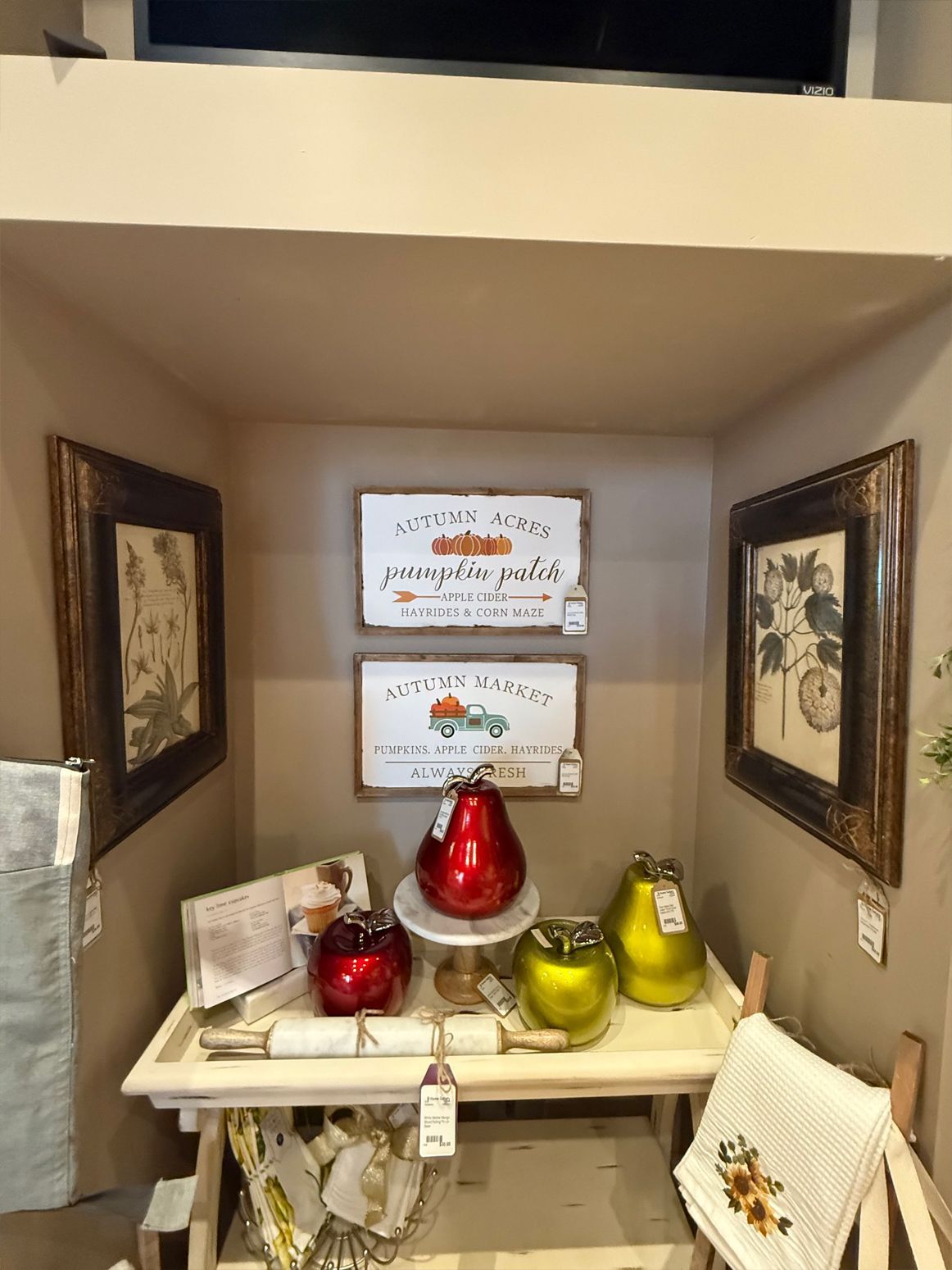 Display of fall-themed decorations: signs, vases, and a towel on a white table in a room with a beige alcove.