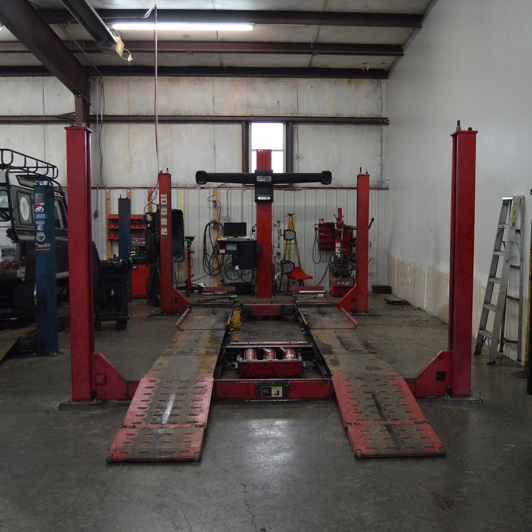 A four-post car lift in a garage. Red columns support ramps on a concrete floor.