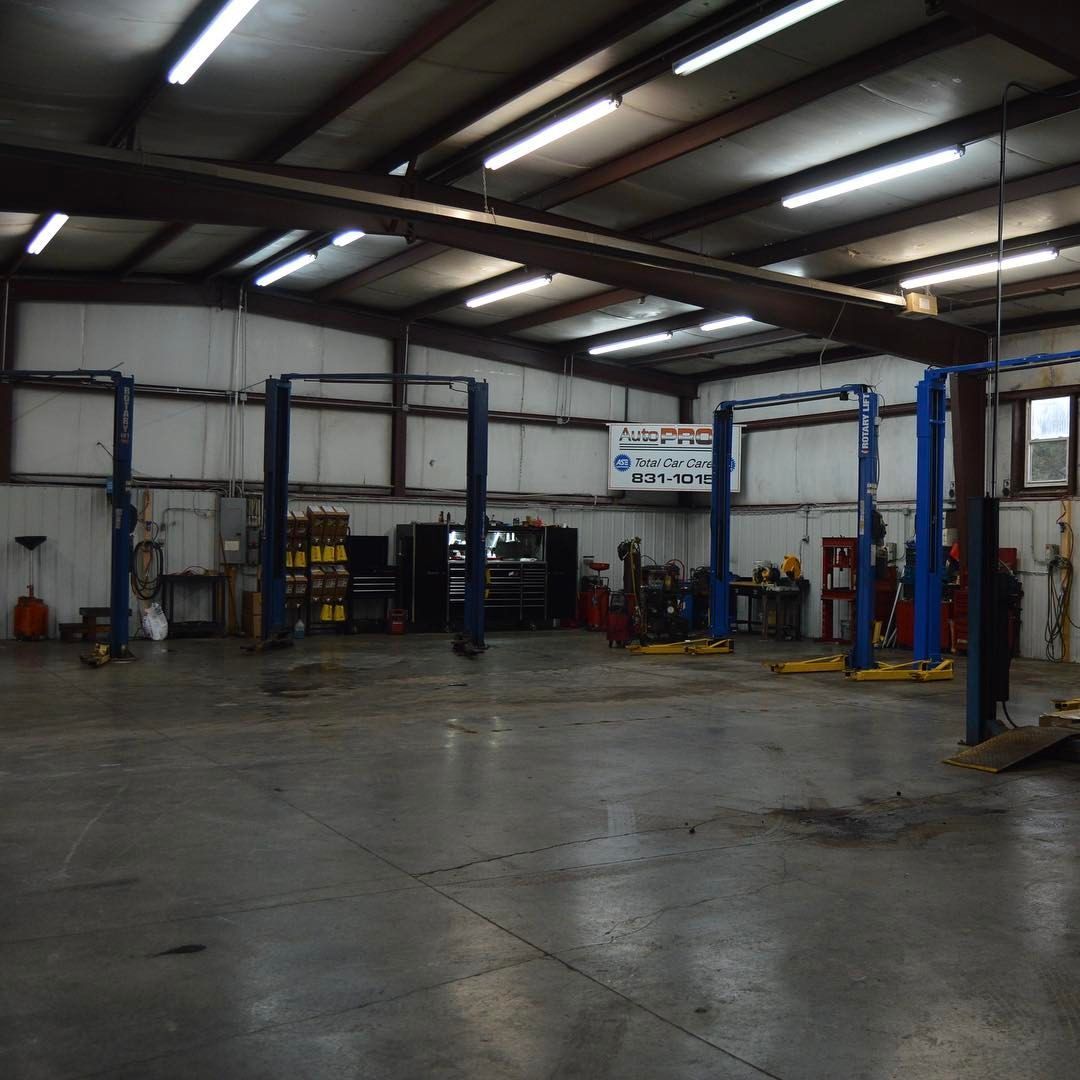 Interior of an auto repair shop with lifts, tools, and a concrete floor under bright fluorescent lights.