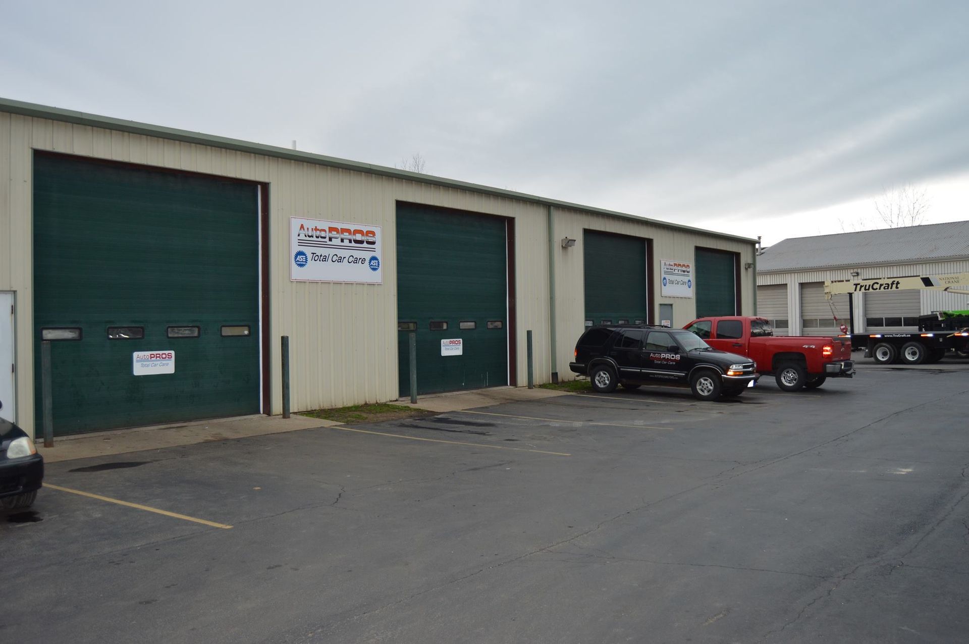 Exterior of a commercial building with three green garage doors; vehicles parked in front.