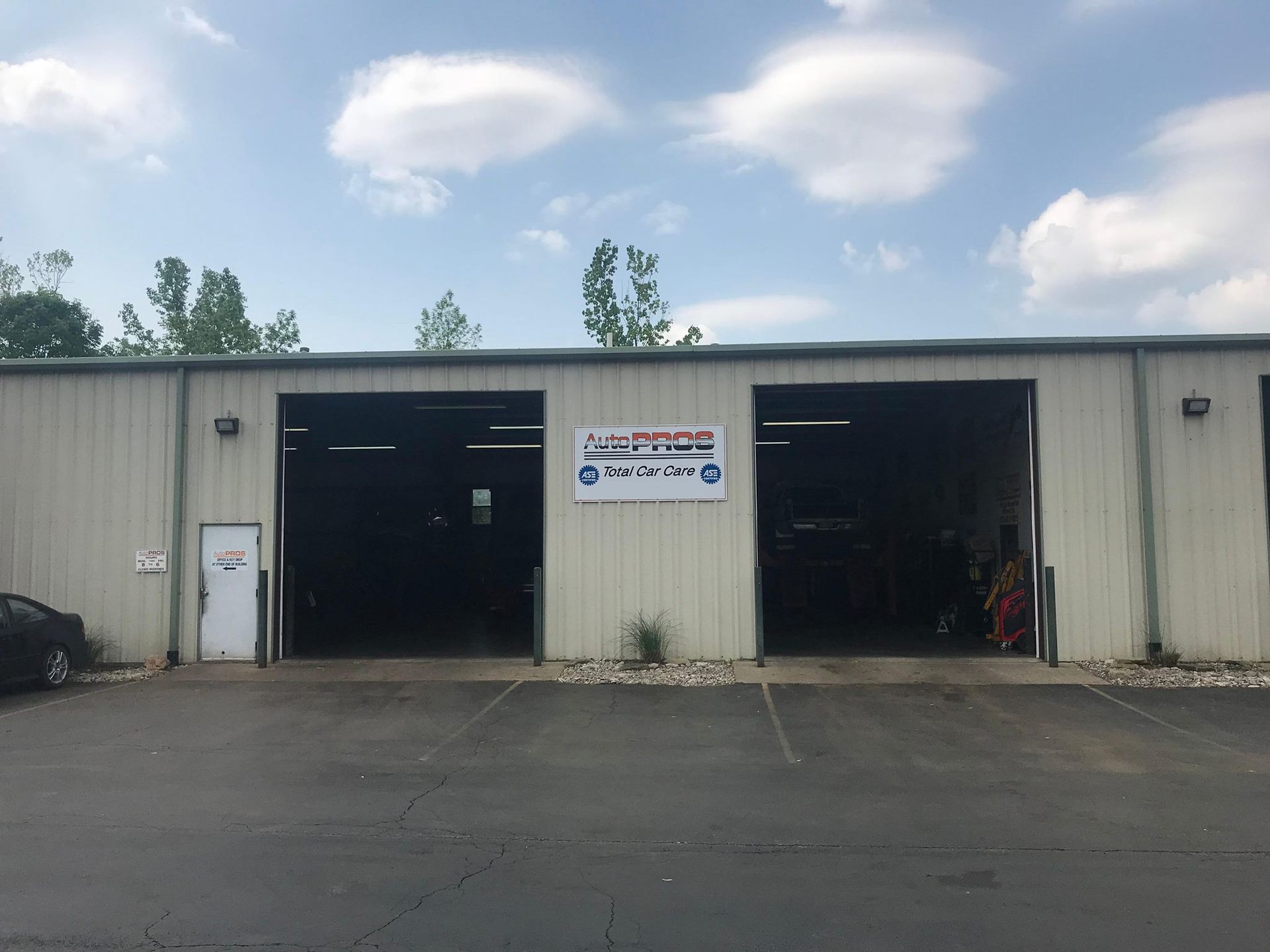 Auto repair shop with two open bays, sign, and small building.