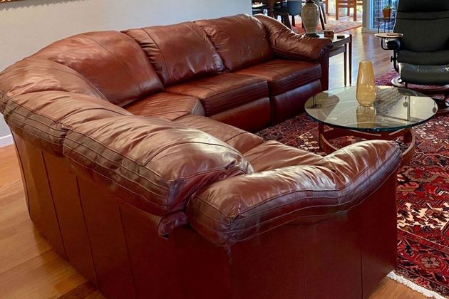 Brown leather sectional sofa beside a glass coffee table on a patterned rug in a living room
