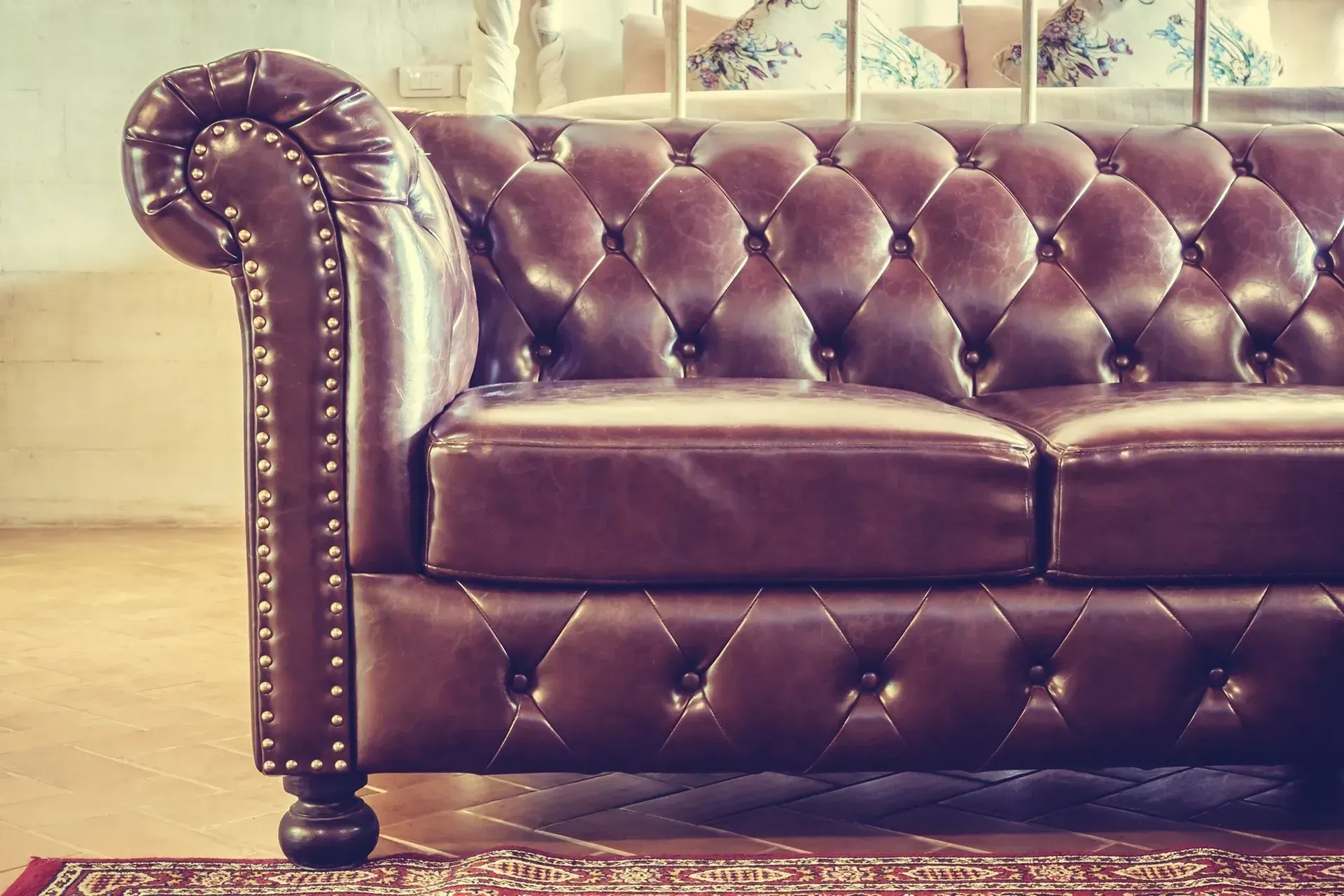 Brown tufted leather sofa against a window, with a rolled arm and nailhead trim