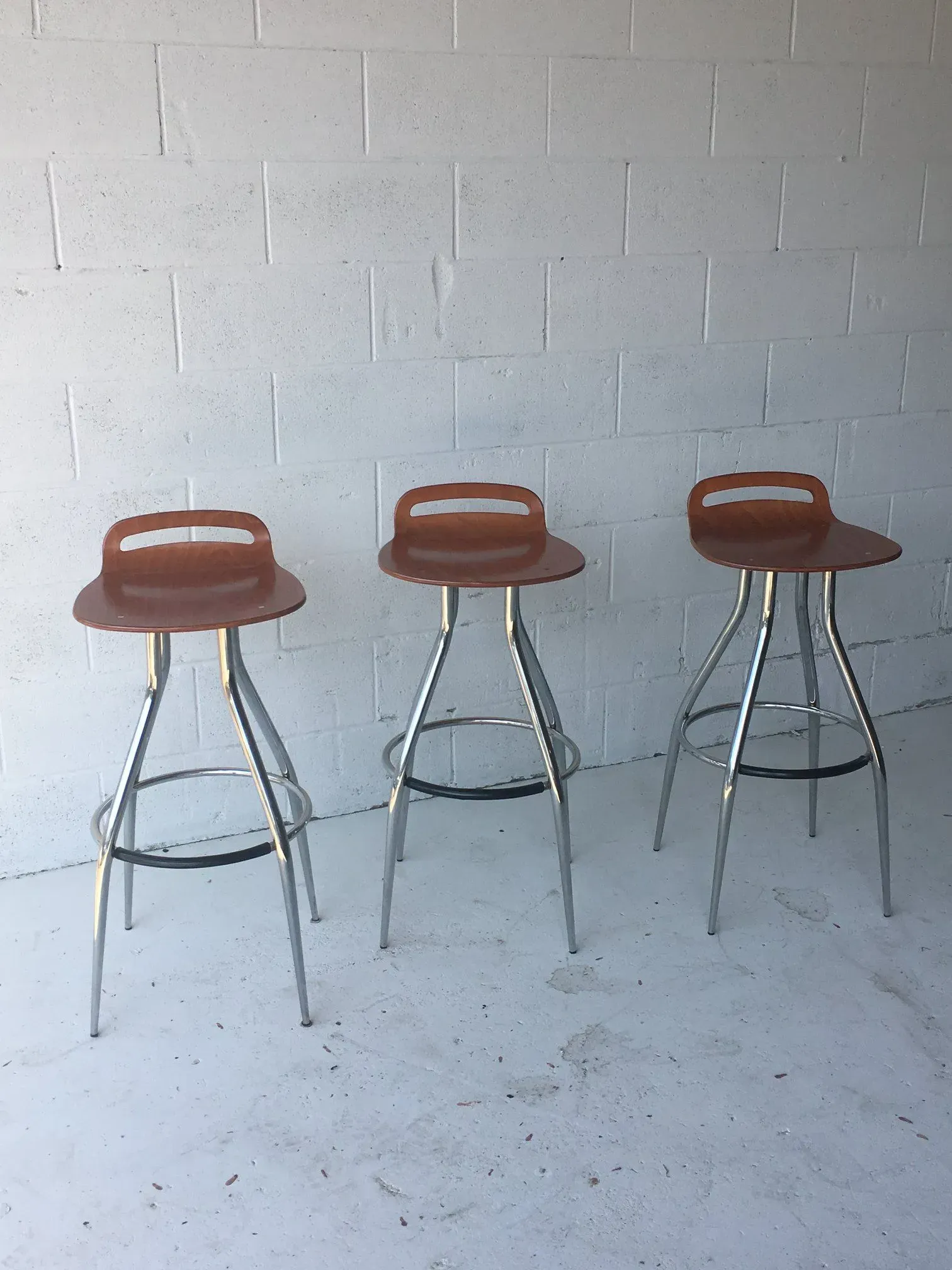 Three brown bar stools with chrome legs against a white brick wall on a concrete floor.