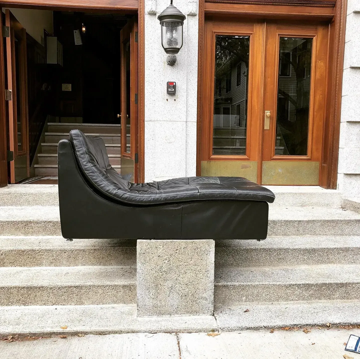 Black chaise lounge on a stone pedestal in front of a building entrance with wooden doors and steps