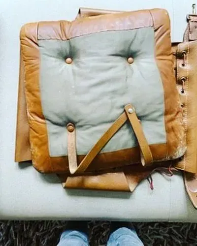 Brown-and-blue padded cushion with straps on a light surface, shown folded or partially open.