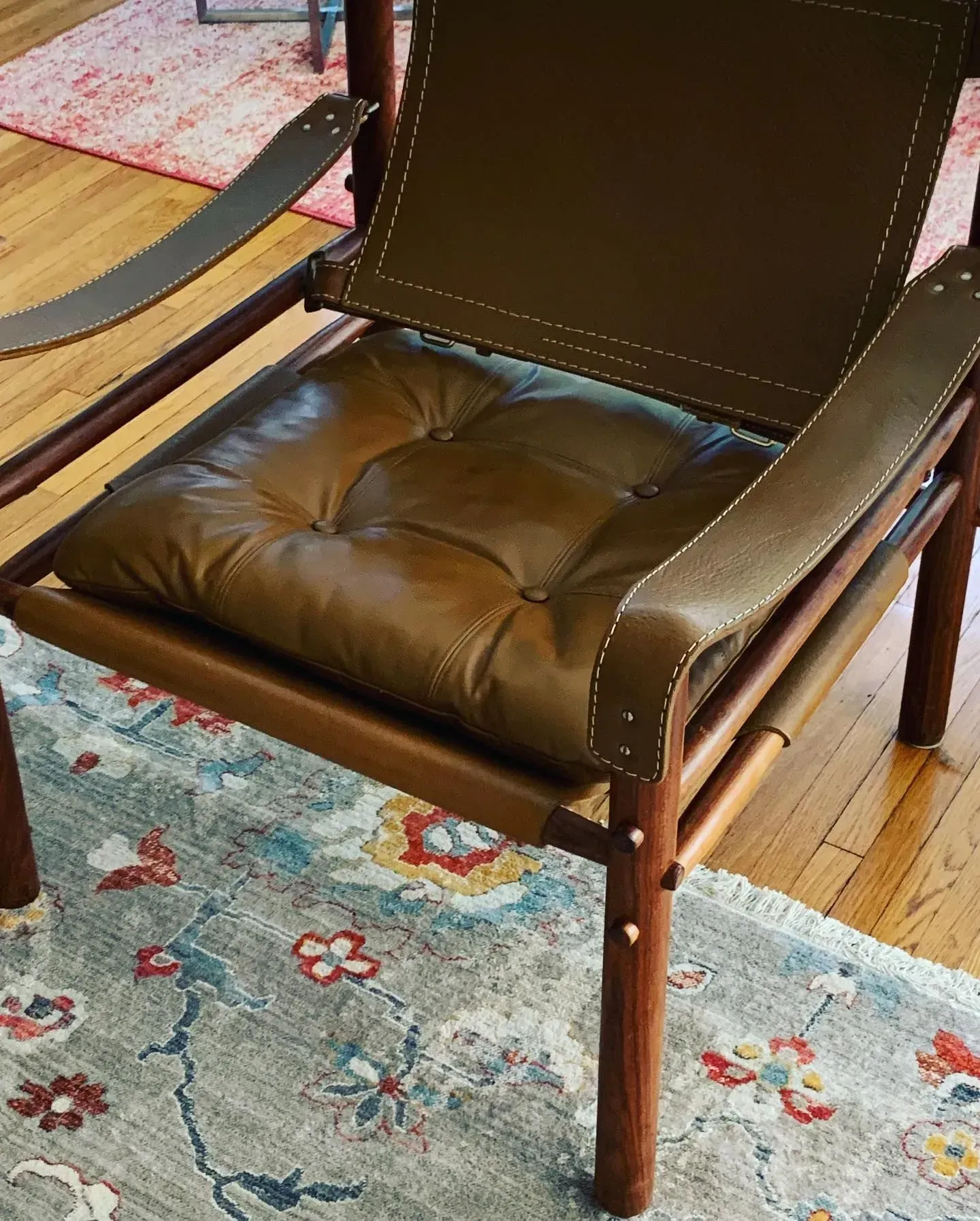 Brown leather cushioned chair with wooden frame on a floral rug in a room with hardwood floor