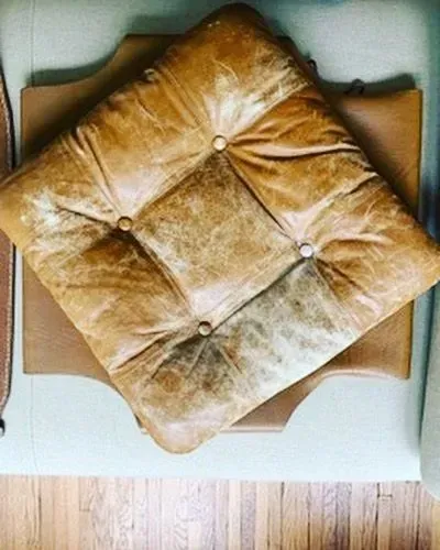 Top view of a gold tufted square cushion on a brown chair, beside a light wood floor.