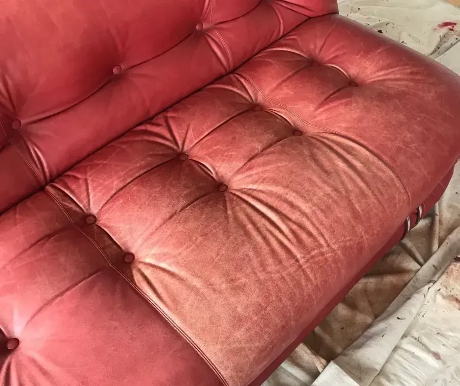 Red tufted cushioned sofa with worn fabric and metal legs on a tiled floor.
