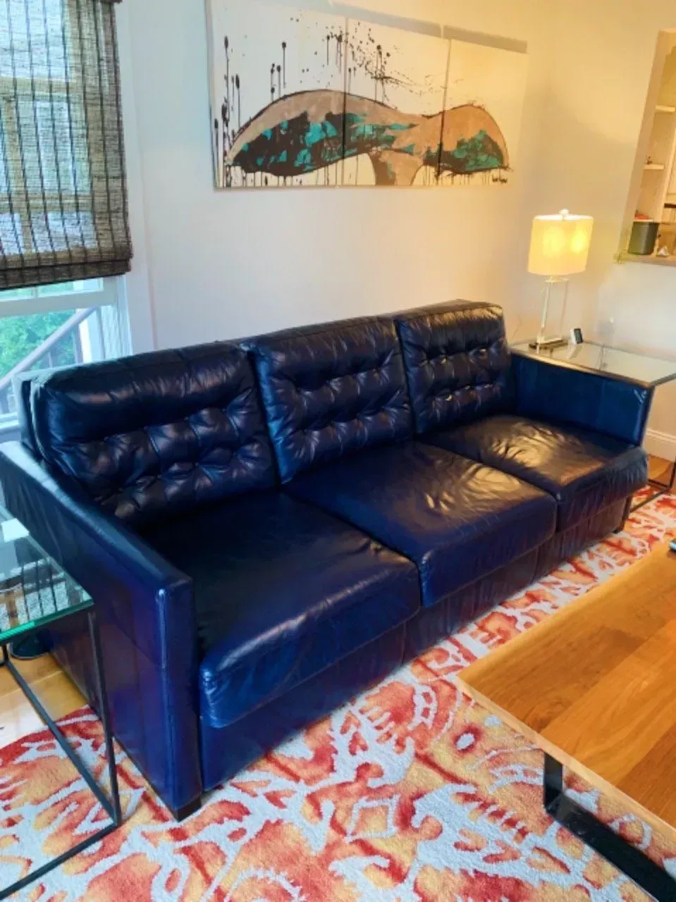 Black leather sofa in a bright living room with a patterned rug and side table lamp.