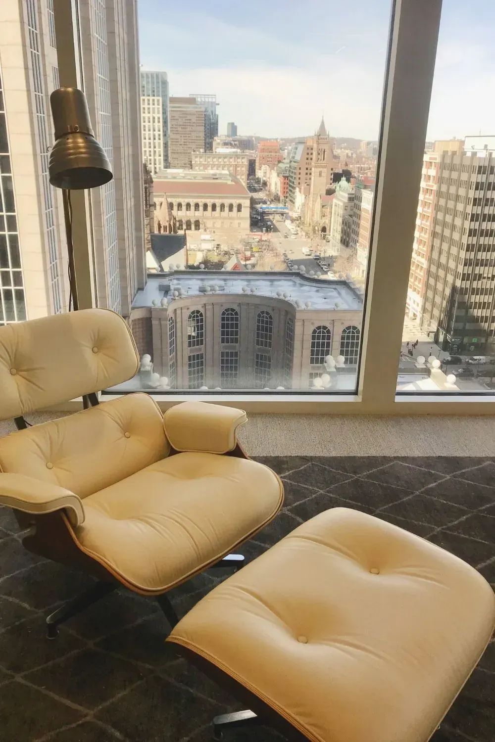 Two tan leather lounge chairs by a large window overlooking a city skyline