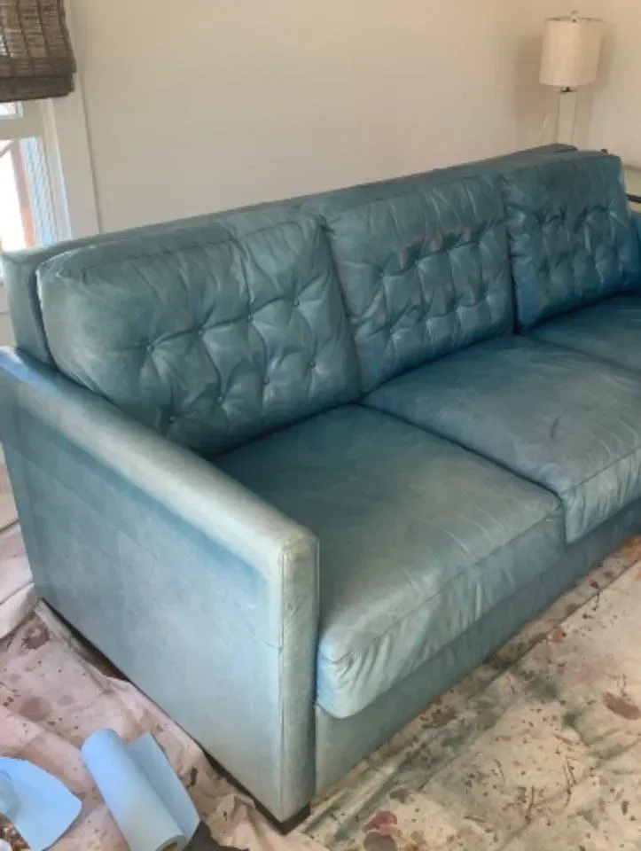 Teal leather sofa in a living room, next to a window and floor lamp.