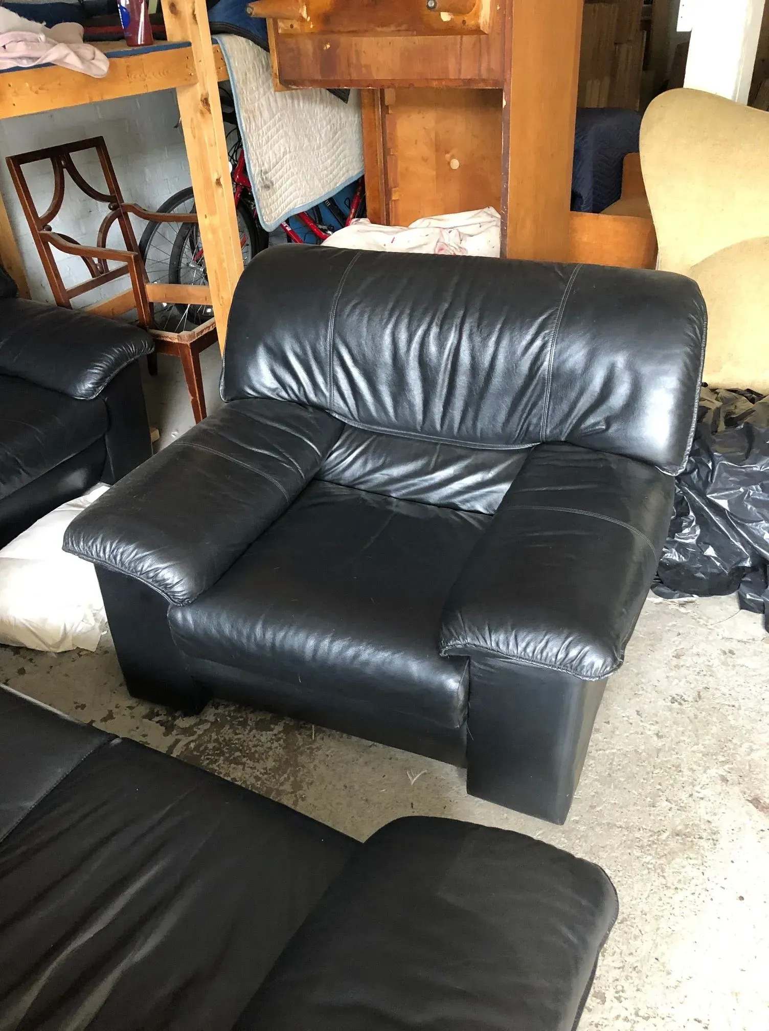 Black leather armchair in a cluttered storage area with wooden furniture and other chairs nearby