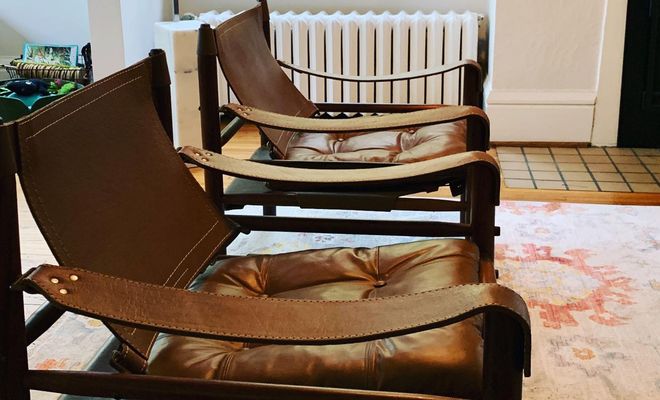Two brown leather chairs in a room with a radiator and patterned rug.