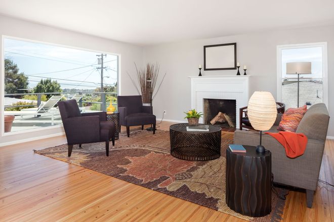 Bright living room with fireplace, large windows, dark chairs, gray sofa, and patterned rug on wood floors