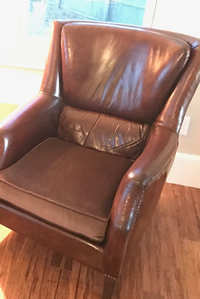 Brown leather armchair by a window on a hardwood floor.