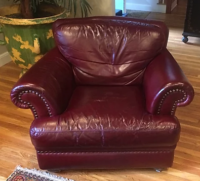 Burgundy leather armchair with rolled arms on a hardwood floor in a living room.