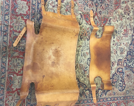 Two worn tan leather pieces laid on a patterned rug, one large and one small.