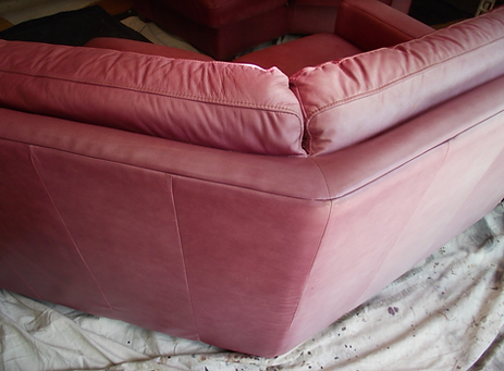Pink upholstered corner sofa with cushions, shown in close-up on a protected floor.