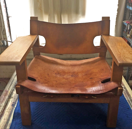Worn wooden armchair with a brown leather seat and back, sitting on a blue rug indoors