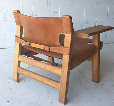 Wooden armchair with brown cushions and side table attached, shown against a white brick wall.