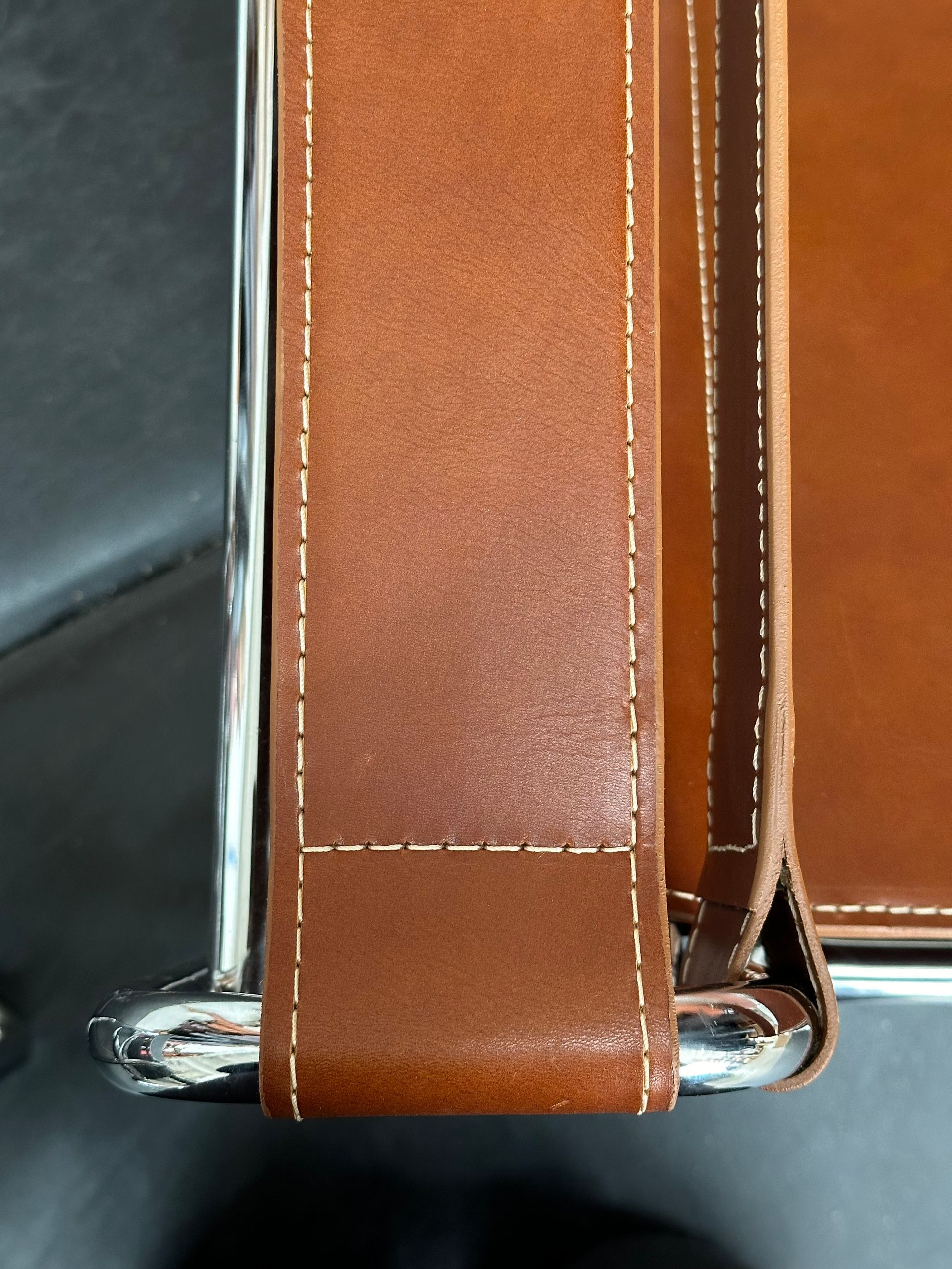 Brown leather strap with white stitching attached to a shiny metal frame
