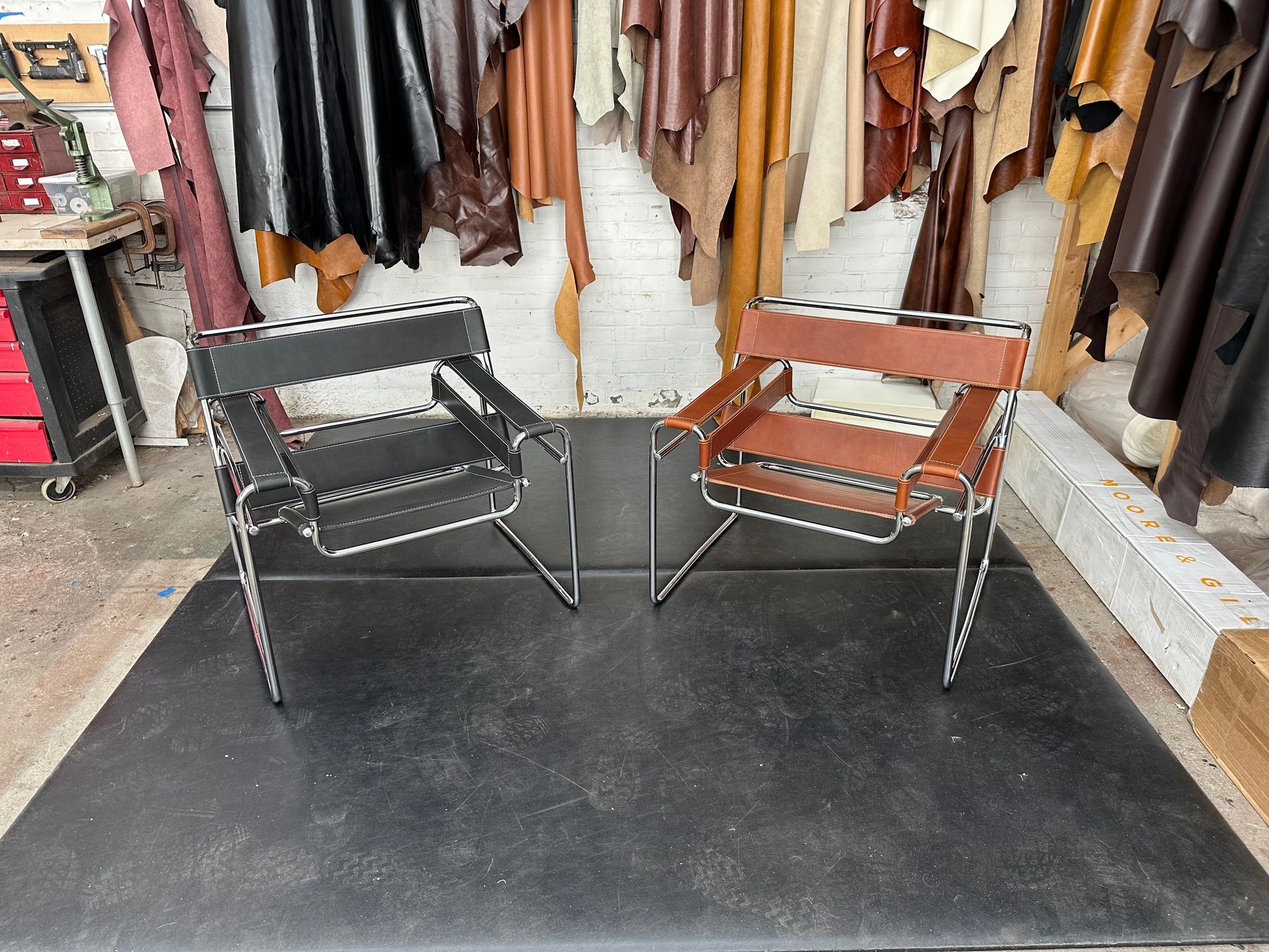 Two folding chairs, one black and one brown, on a black mat in a leather shop