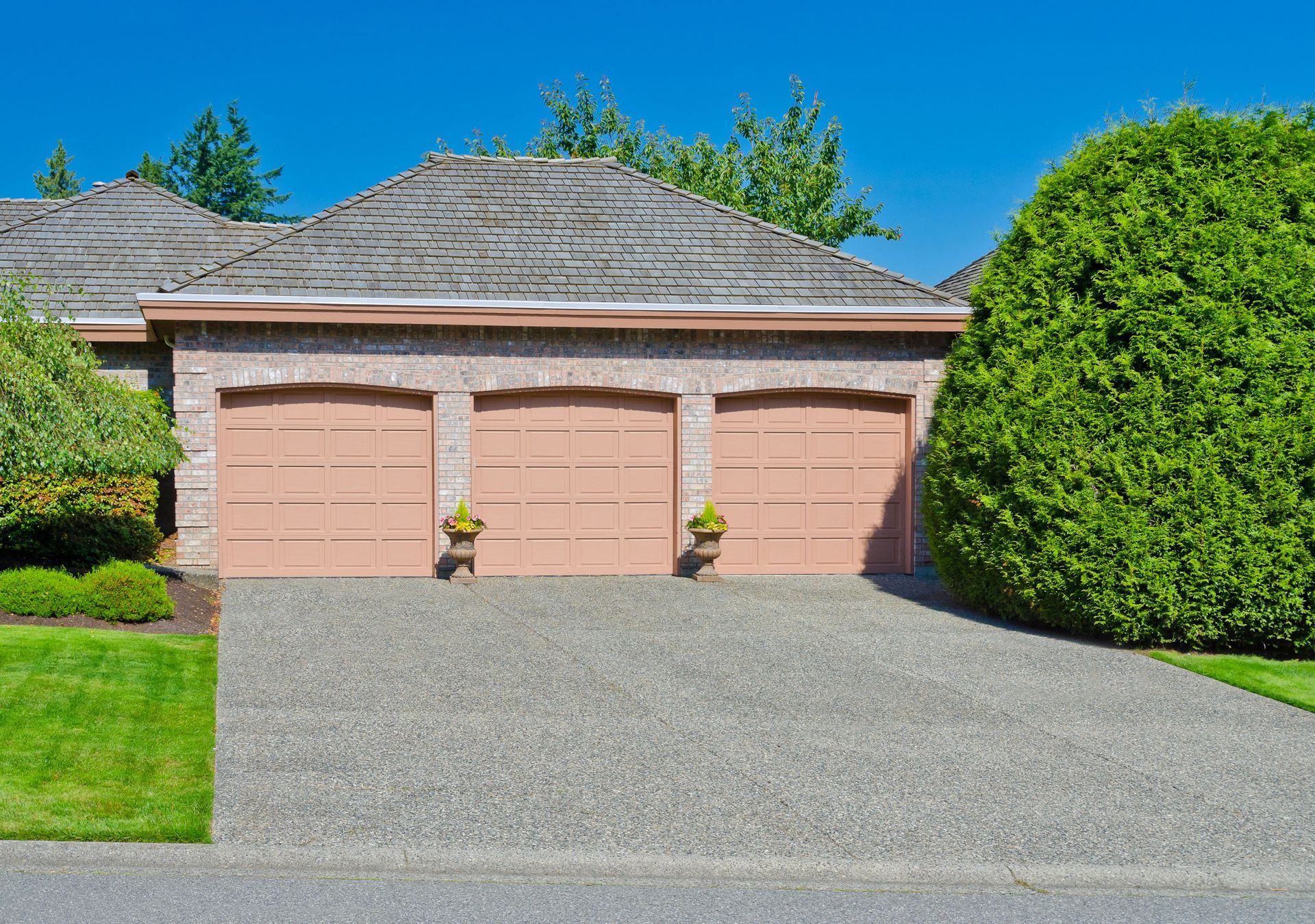 Three-car garage with peach-colored doors, brick exterior, and gravel driveway under a blue sky.