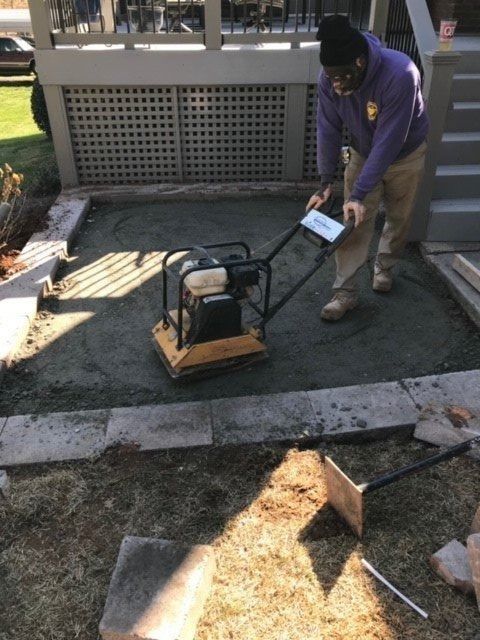 Person operating a plate compactor on a gravel surface; outdoor setting.