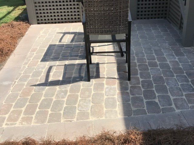 Patio with gray paving stones, surrounded by a darker border, a wicker chair sits on the patio.
