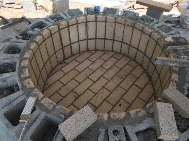 Circular brick fire pit under construction, using light-colored bricks and mortar.