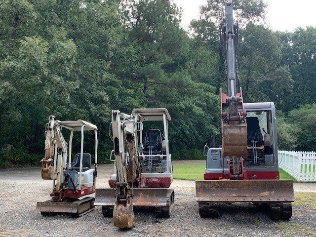 Three mini excavators parked on gravel, lined up with different sizes.