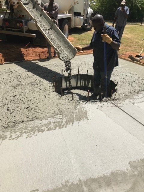 Workers pouring concrete from a truck into a hole, creating a sidewalk in an outdoor setting.