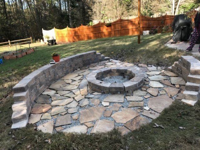 Stone fire pit area with curved seating in a backyard setting.