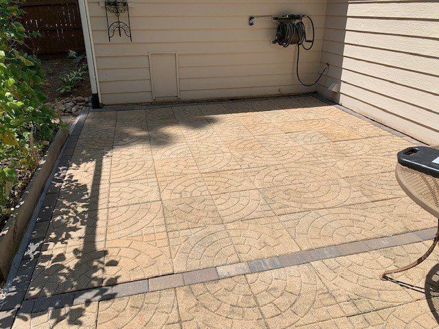 Tan patio with patterned pavers, against a cream-colored wall. A garden table sits on the right.