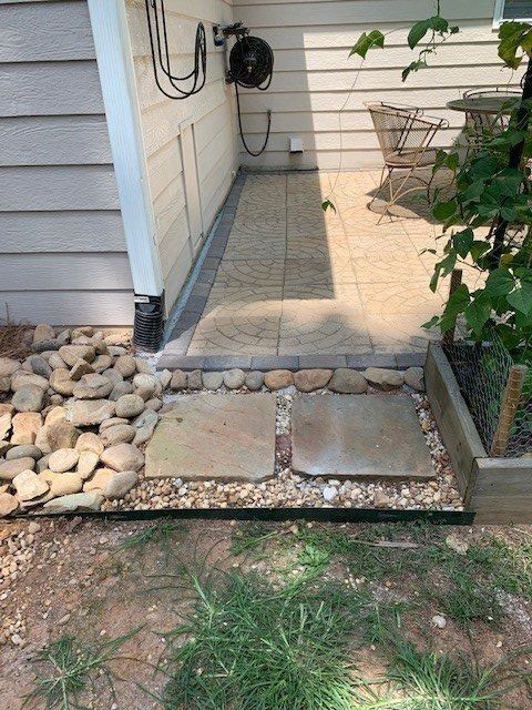Stone walkway and patio next to a house with a small rock garden and two stepping stones.