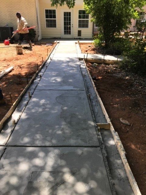 Construction of a concrete walkway; a worker levels the wet concrete in a yard next to a building.