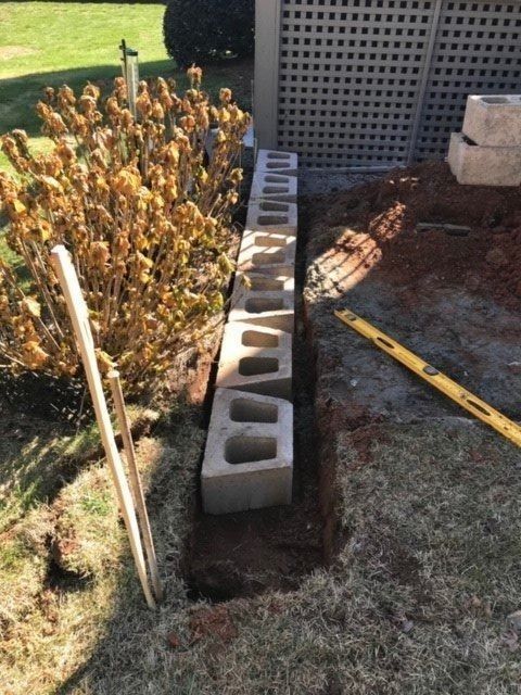 Concrete blocks being placed in a trench to build a retaining wall in a yard.