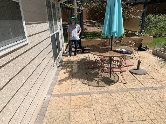 Person in blue hat stands on a patterned patio near a table with an umbrella.