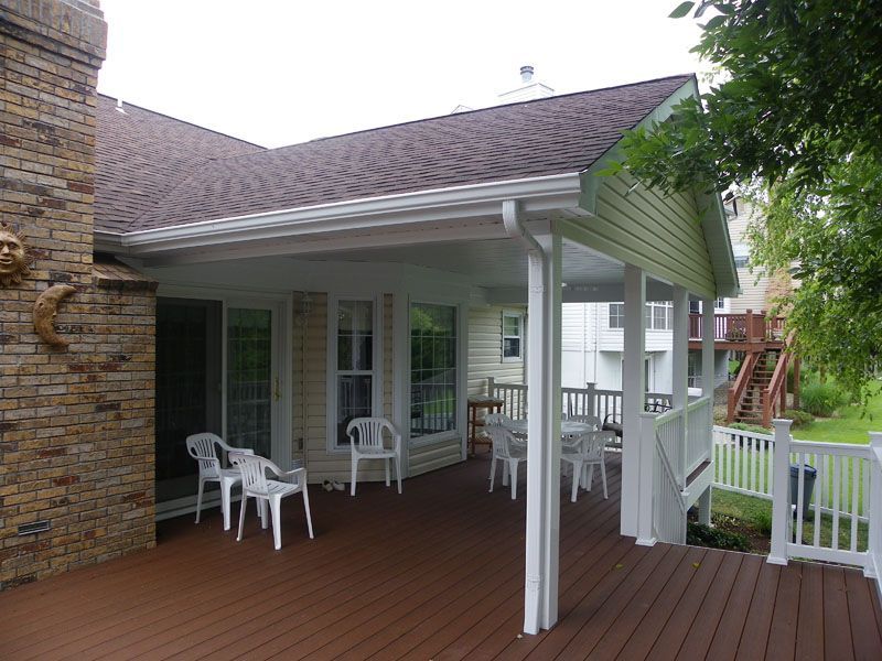 a covered deck with chairs and tables in front of a house