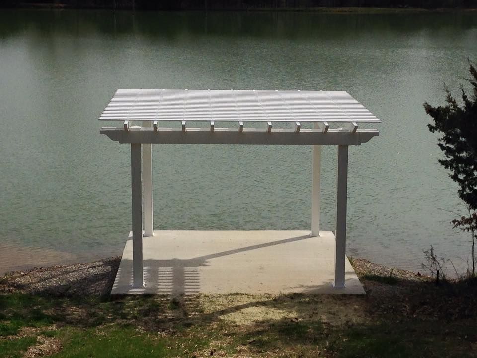 a white pergola sits on the shore of a lake