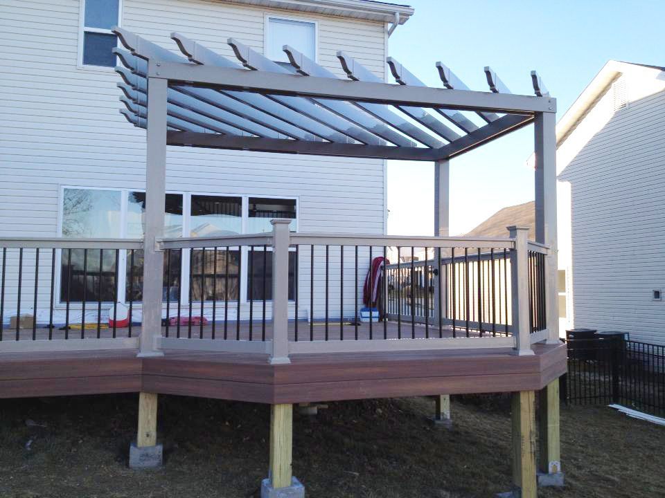 a deck with a pergola and railing in front of a house