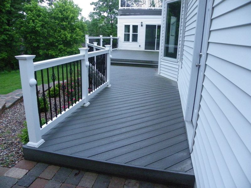 a gray deck with a white railing next to a white house