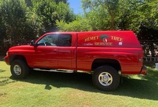 Red pickup truck with Hemet Tree Service logo, parked on grass.