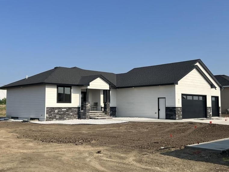 A white house with a black roof is sitting on top of a dirt field.