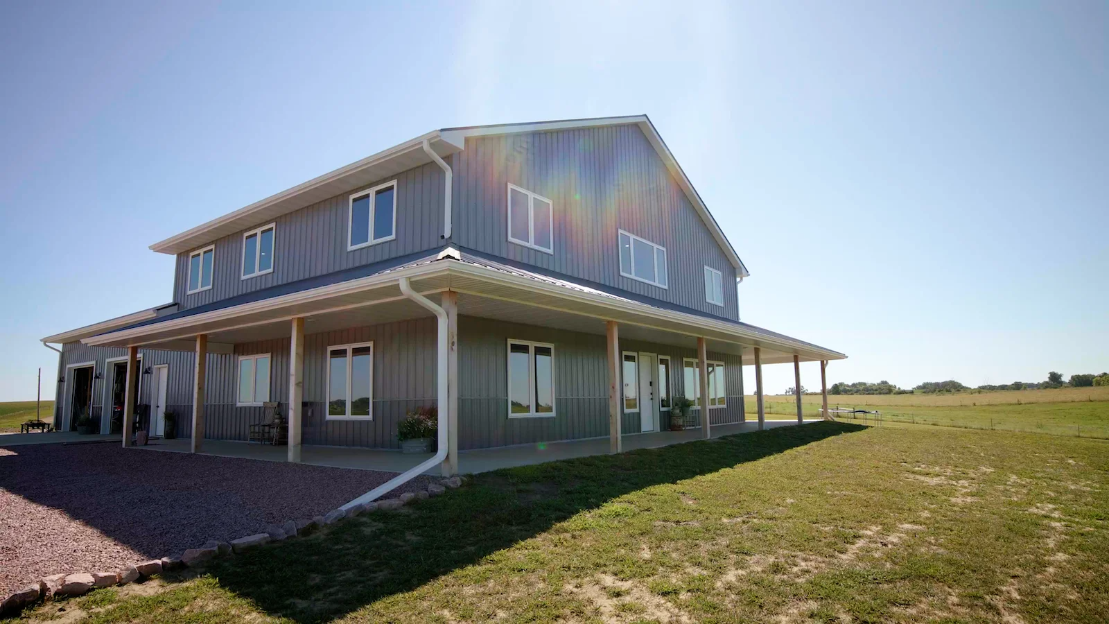 A large house with a porch is sitting in the middle of a grassy field.