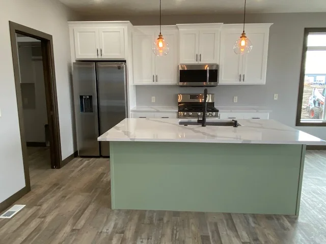 A kitchen with white cabinets , stainless steel appliances and a large island.