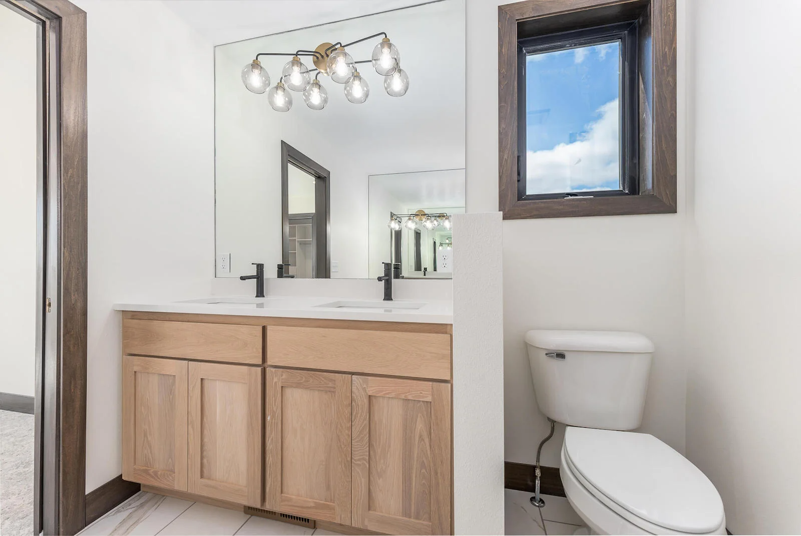 A bathroom with a toilet , sink , mirror and window.